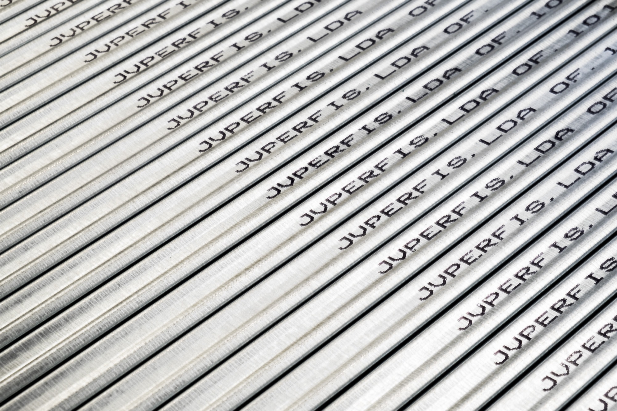 Macro de perfis galvanizados na diagonal, cada um com a marcação impressa «JVPERFIS, LDA OF. 10» repetida ao longo do aço.